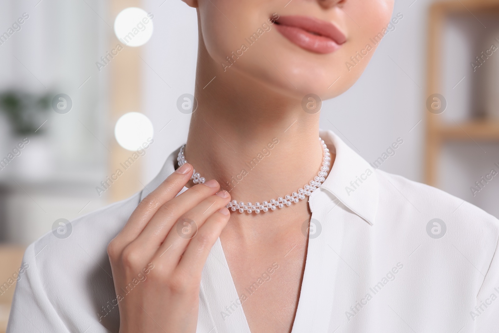 Photo of Young woman trying on elegant pearl necklace indoors, closeup