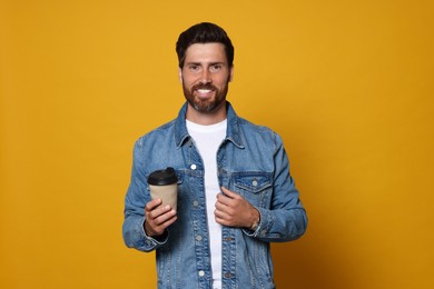 Photo of Smiling bearded man with paper cup of drink on orange background