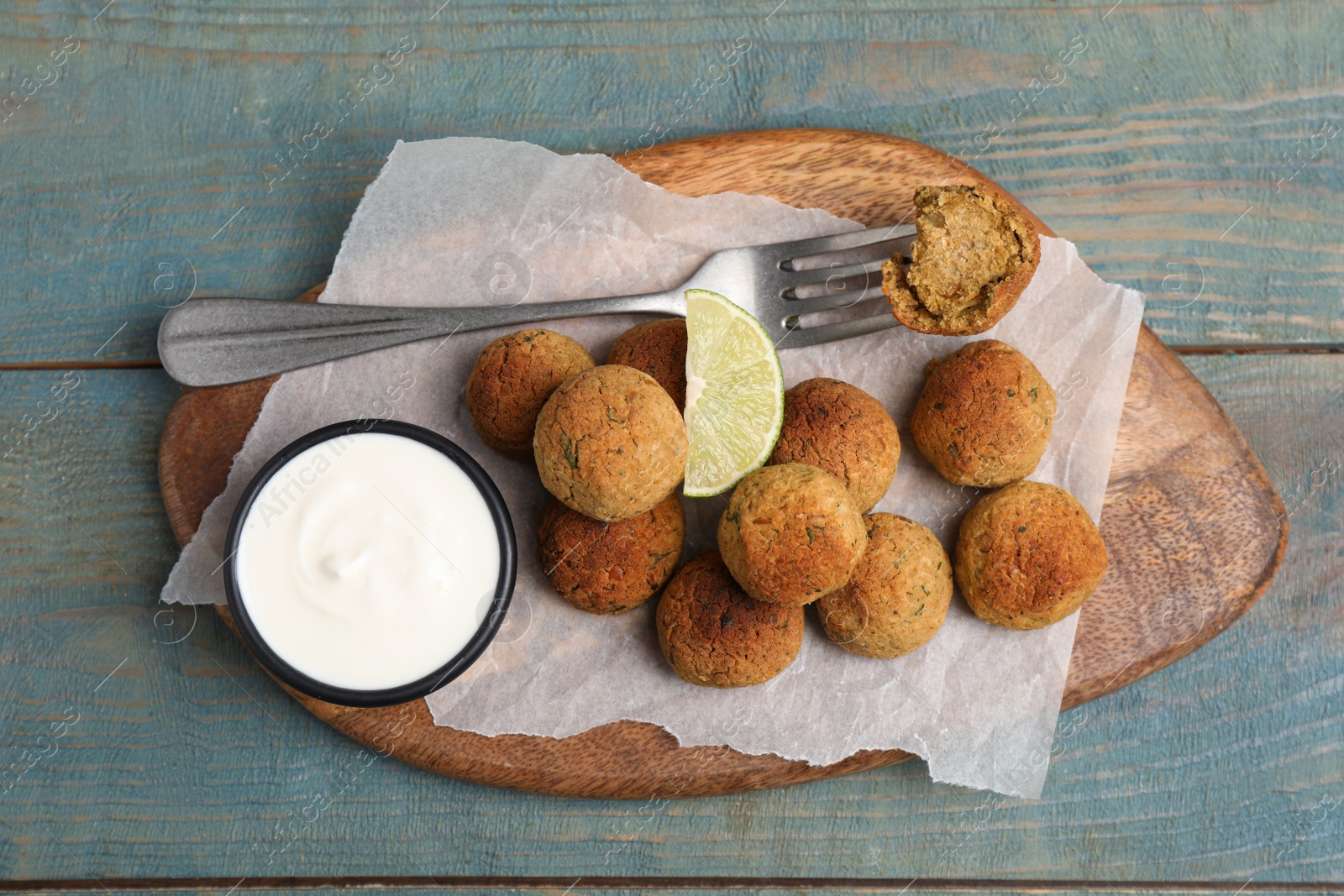 Photo of Delicious falafel balls with lime and sauce on light blue wooden table, top view