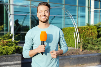 Young male journalist with microphone working on city street