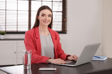 Photo of Young businesswoman using laptop at table in office