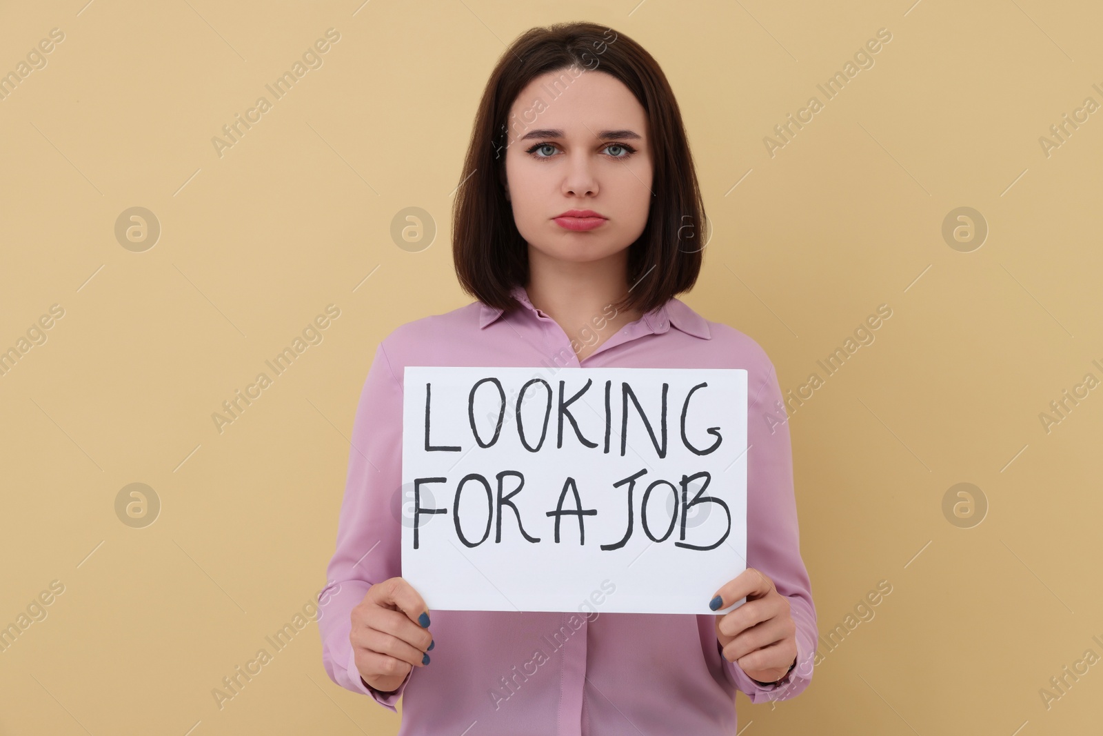 Photo of Young unemployed woman holding sign with phrase Looking For A Job on beige background