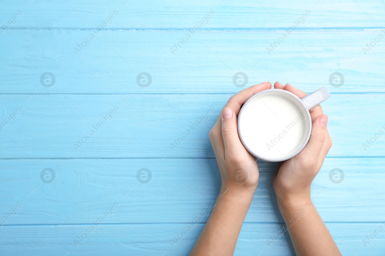 Photo of Woman holding glass of milk on wooden table, top view. Space for text