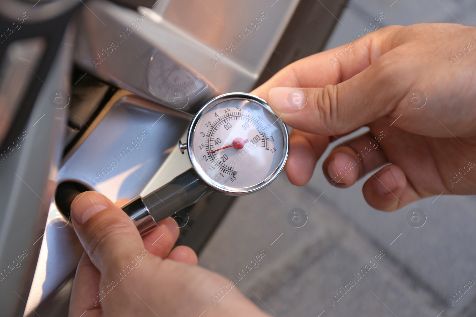 Photo of Man checking air pressure in car tire outdoors, closeup