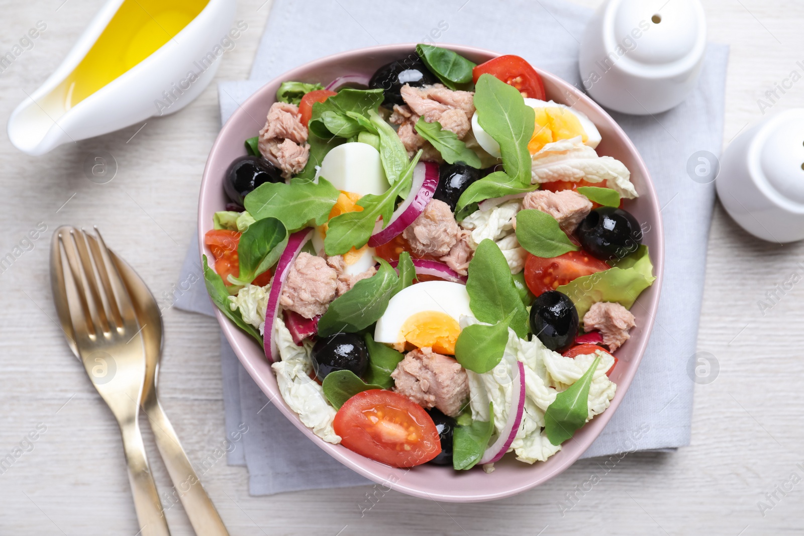 Photo of Bowl of delicious salad with canned tuna and vegetables served on white wooden table, flat lay