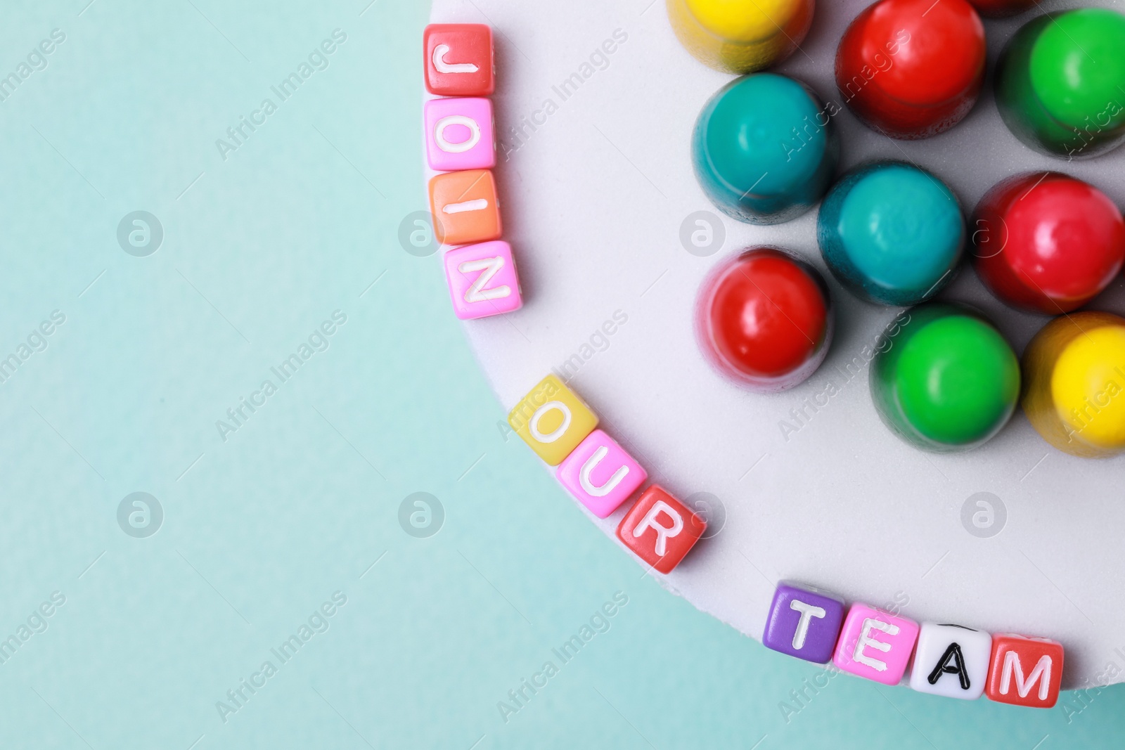 Photo of Colorful cubes with phrase Join Our Team and pawns on light blue background, flat lay with space for text. Recruiter searching employee