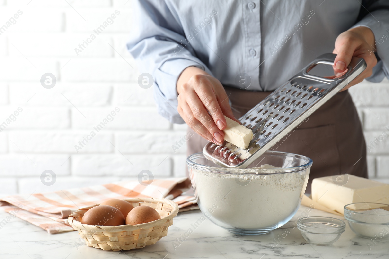 Photo of Woman grating butter into bowl with flour at white marble table, closeup