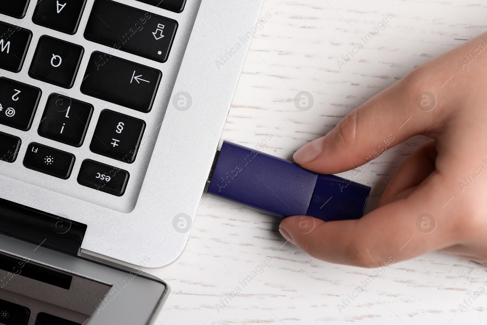 Photo of Woman attaching usb flash drive into laptop at white wooden table, top view