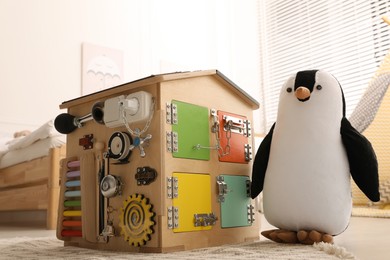 Busy board house and toy penguin on floor indoors