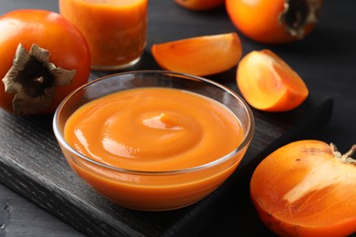 Delicious persimmon jam in glass bowl and fresh fruits on dark gray wooden table, closeup