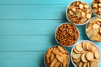 Different delicious crackers in bowls on turquoise wooden table, flat lay. Space for text