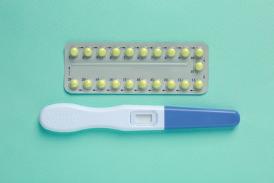 Photo of Birth control pills and pregnancy test on light blue background, top view