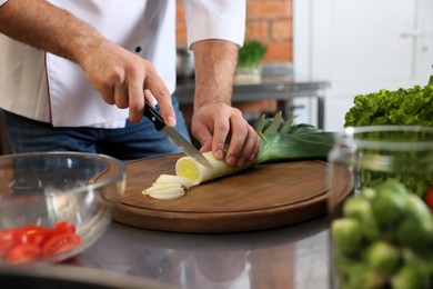 Photo of Professional chef cutting fresh leek in restaurant kitchen, closeup