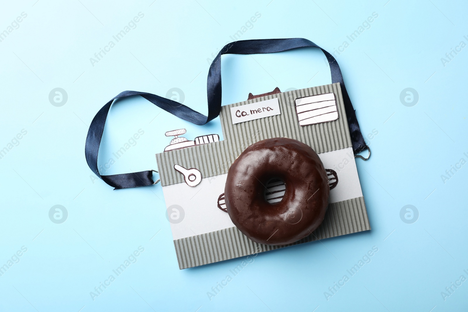Photo of Camera made from donut and piece of cardboard on light blue background, top view