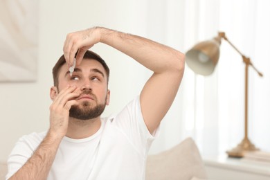 Photo of Young man using eye drops in room