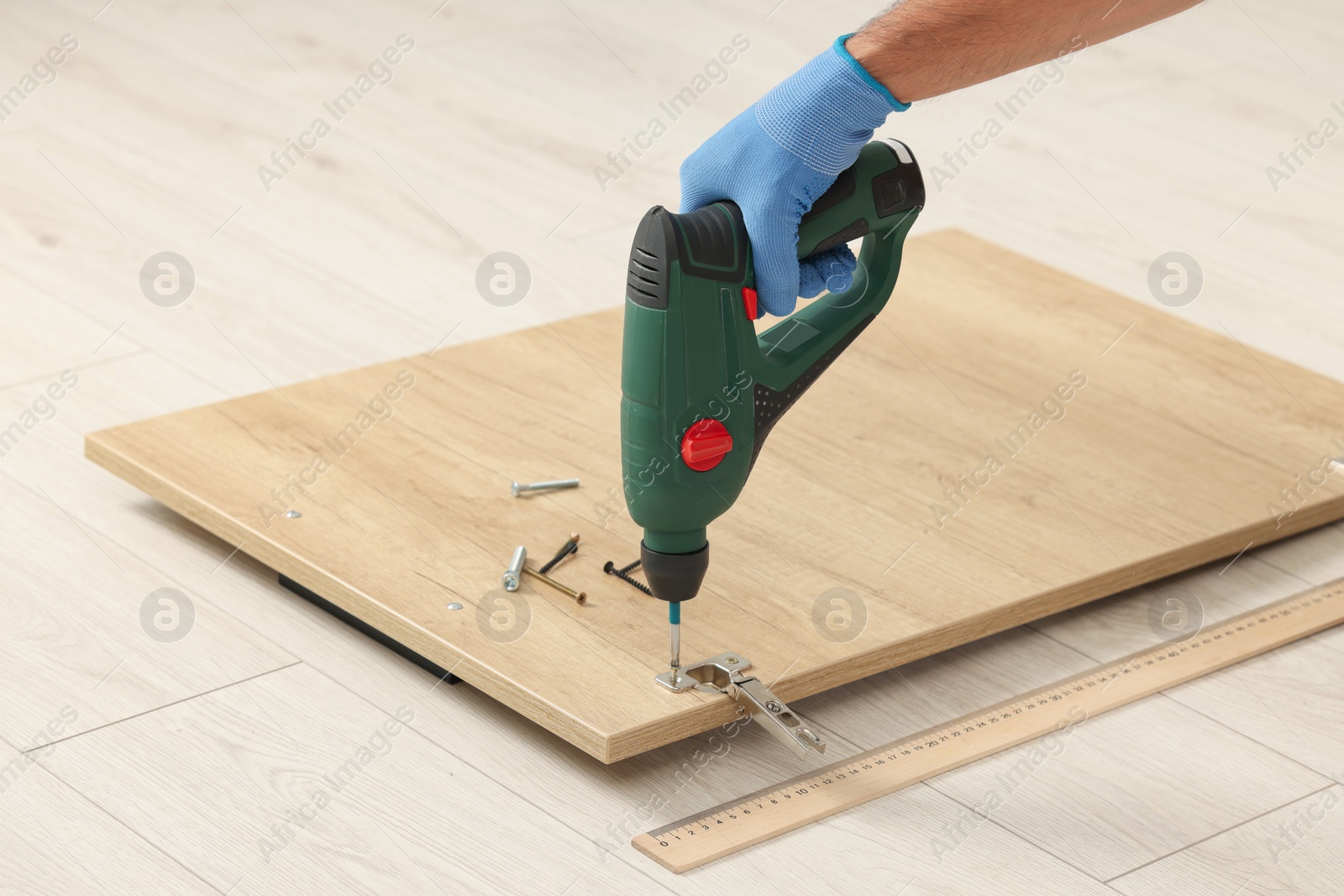 Photo of Man with electric screwdriver assembling furniture on floor, closeup