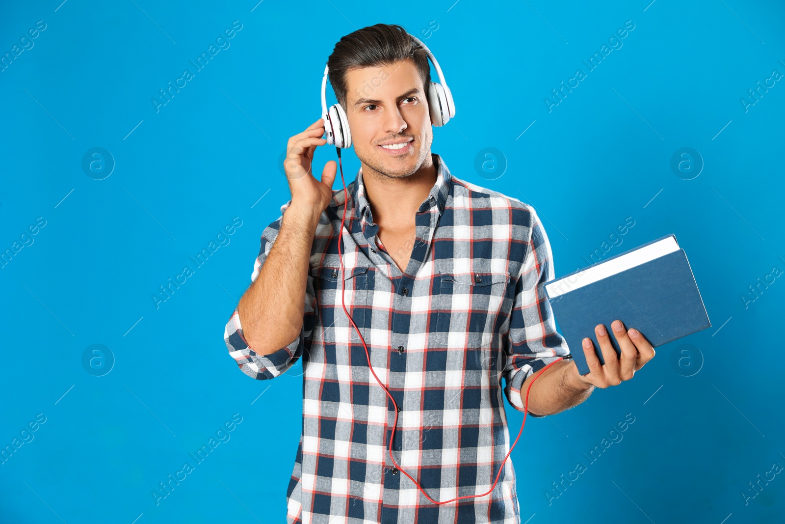 Photo of Man with headphones and book on light blue background. Audiobook concept