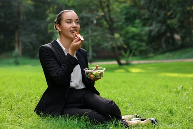 Lunch time. Happy businesswoman eating salad on green grass in park