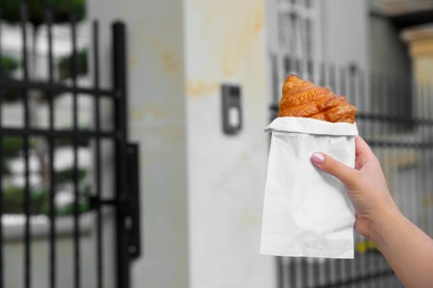 Photo of Woman holding croissant in hand near gate outdoors, closeup. Space for text