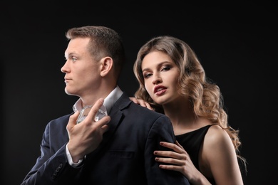 Passionate woman and handsome man using perfume on black background