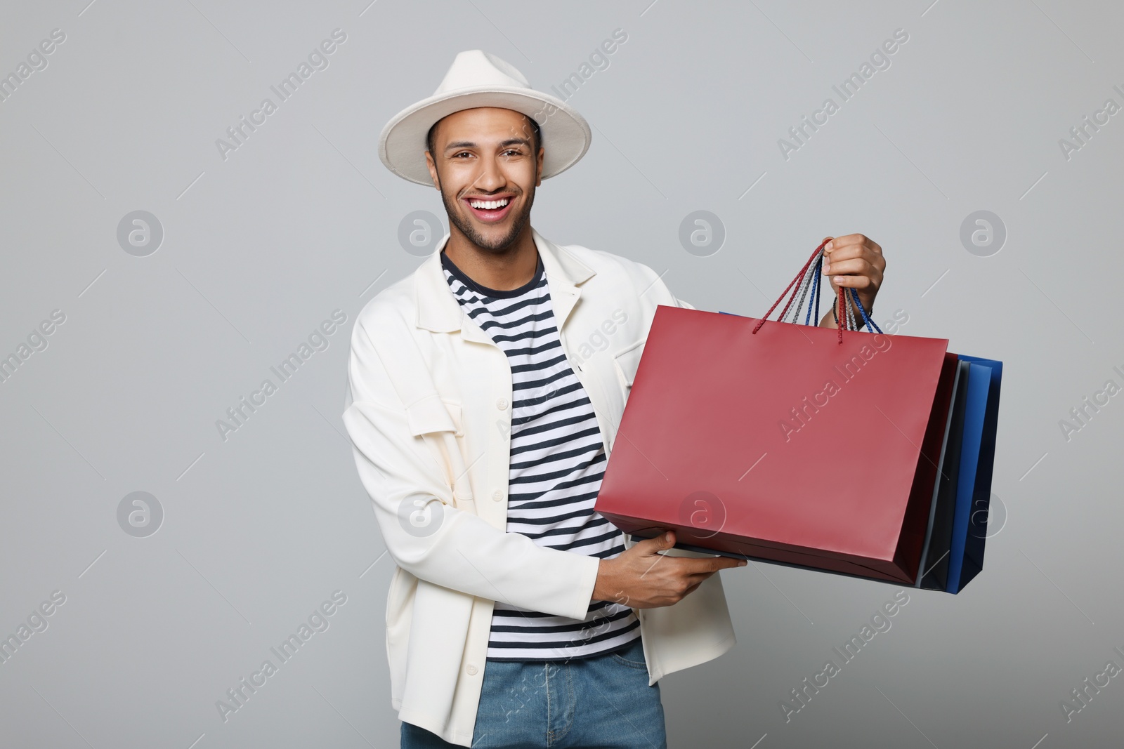 Photo of Happy African American man in hat with shopping bags on light grey background