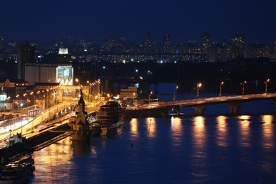 KYIV, UKRAINE - MAY 21, 2019: Beautiful view of night cityscape with illuminated buildings near river and bridge