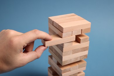 Playing Jenga. Man removing wooden block from tower on blue background, closeup