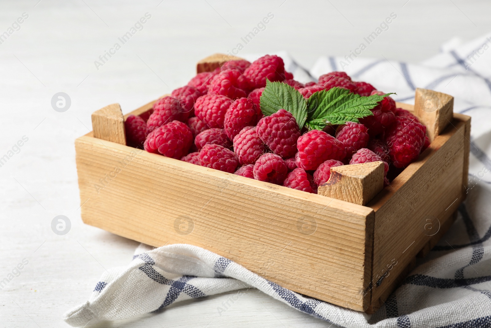 Photo of Crate of delicious fresh ripe raspberries with leaves on white wooden table