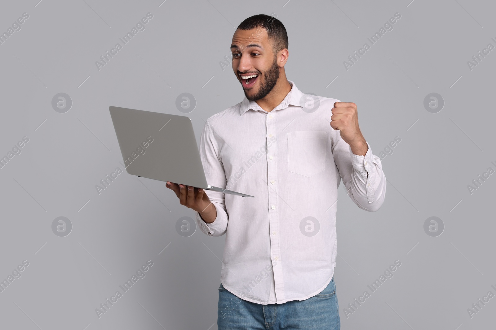 Photo of Happy young man with laptop on grey background. Space for text