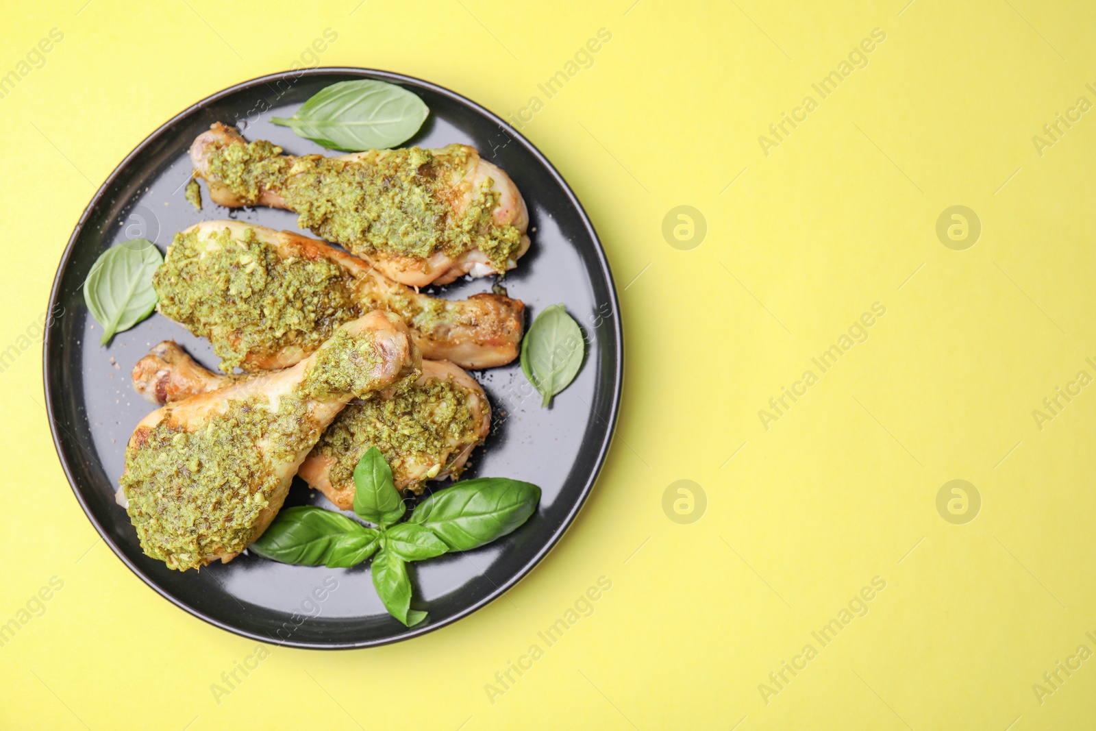 Photo of Delicious fried chicken drumsticks with pesto sauce and basil on yellow table, top view. Space for text