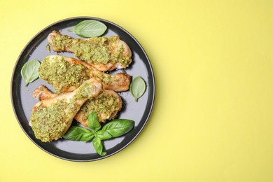 Delicious fried chicken drumsticks with pesto sauce and basil on yellow table, top view. Space for text