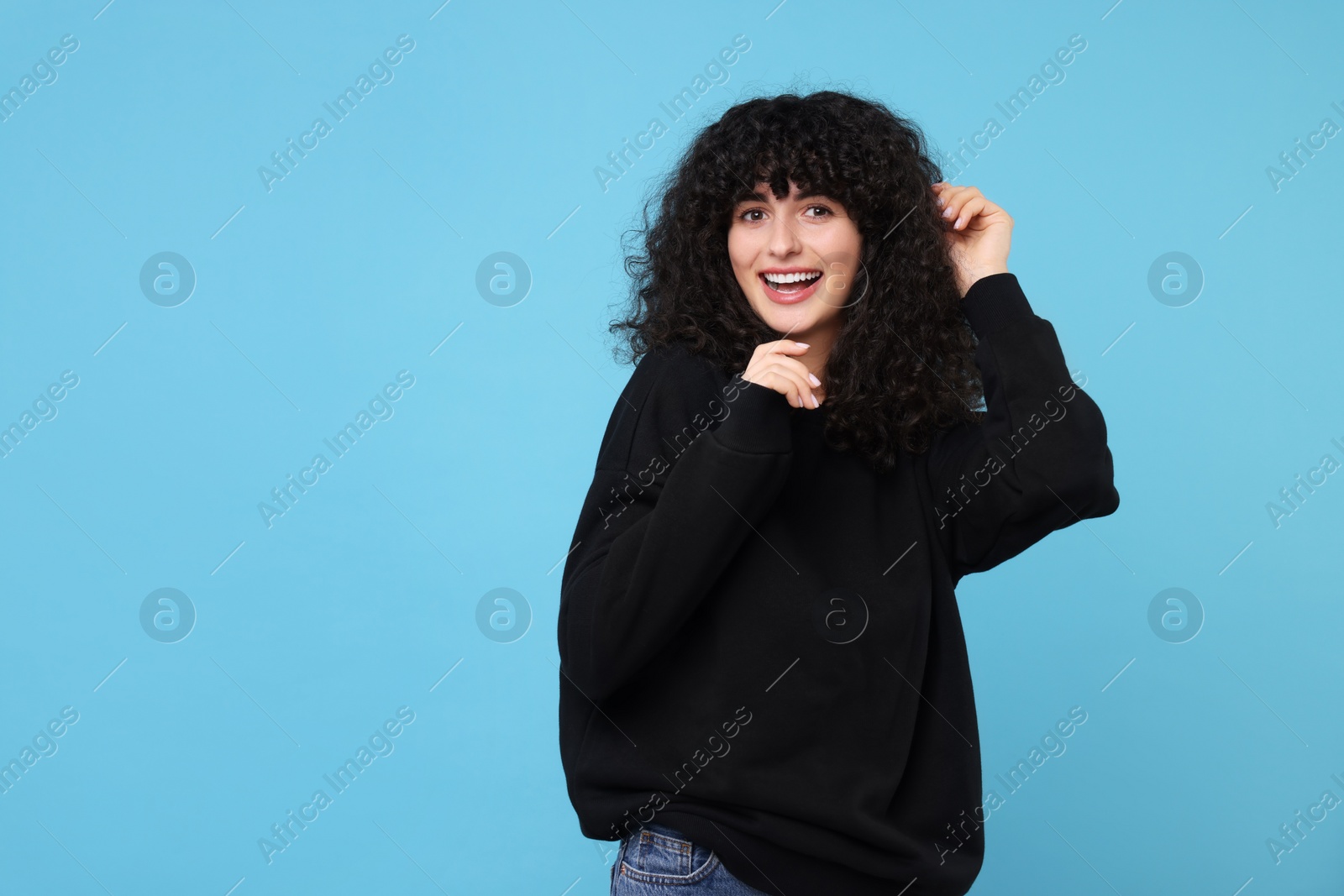 Photo of Happy young woman in stylish black sweater on light blue background, space for text