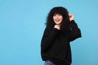 Photo of Happy young woman in stylish black sweater on light blue background, space for text