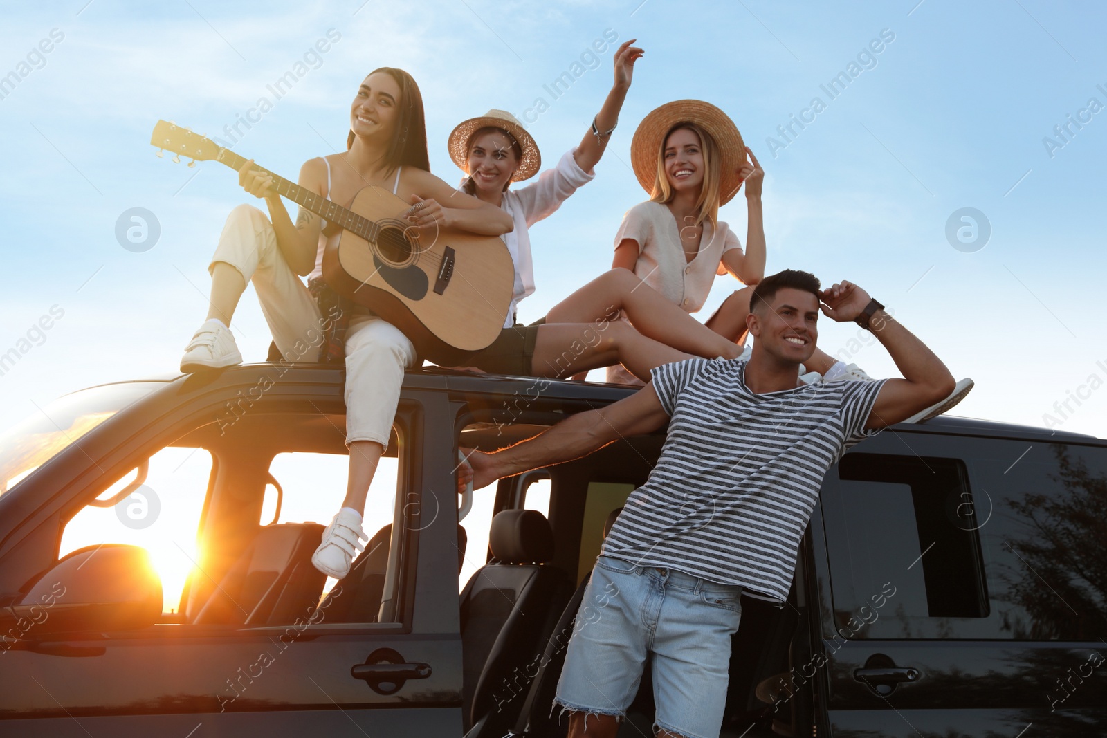 Photo of Happy friends with guitar outdoors at sunset. Summer trip