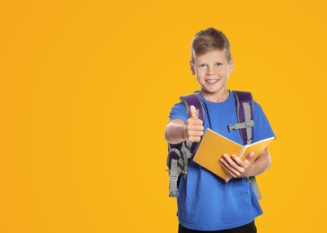 Cute boy with school stationery showing thumbs up on yellow background, space for text