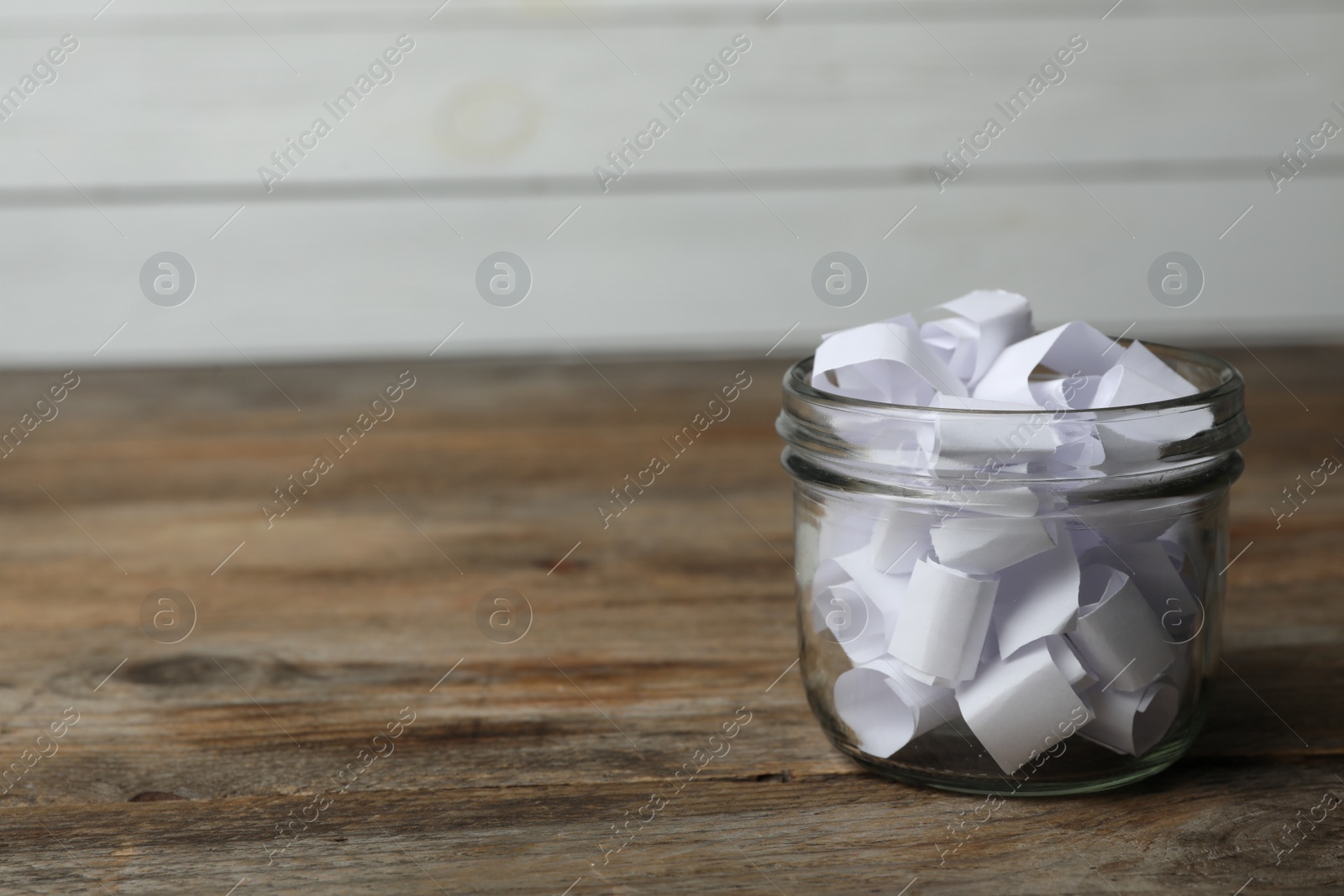 Photo of Glass jar with paper pieces on wooden table, space for text