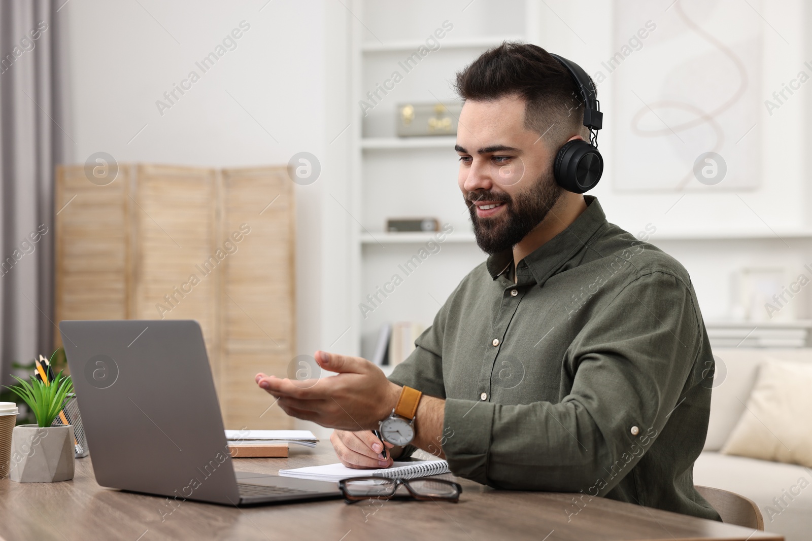 Photo of E-learning. Young man using laptop during online lesson at wooden table indoors