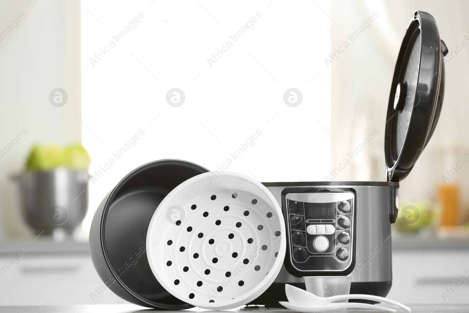 Photo of Modern electric multi cooker, parts and accessories on table in kitchen. Space for text