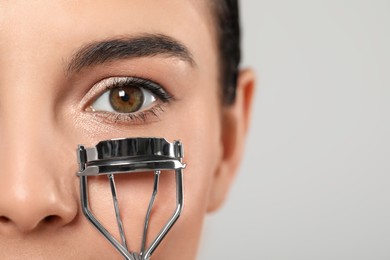 Photo of Young woman using eyelash curler on light grey background, closeup. Space for text