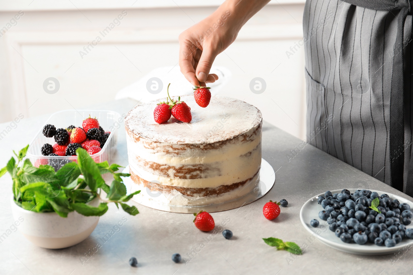 Photo of Woman decorating delicious cake with fresh berries at table. Homemade pastry