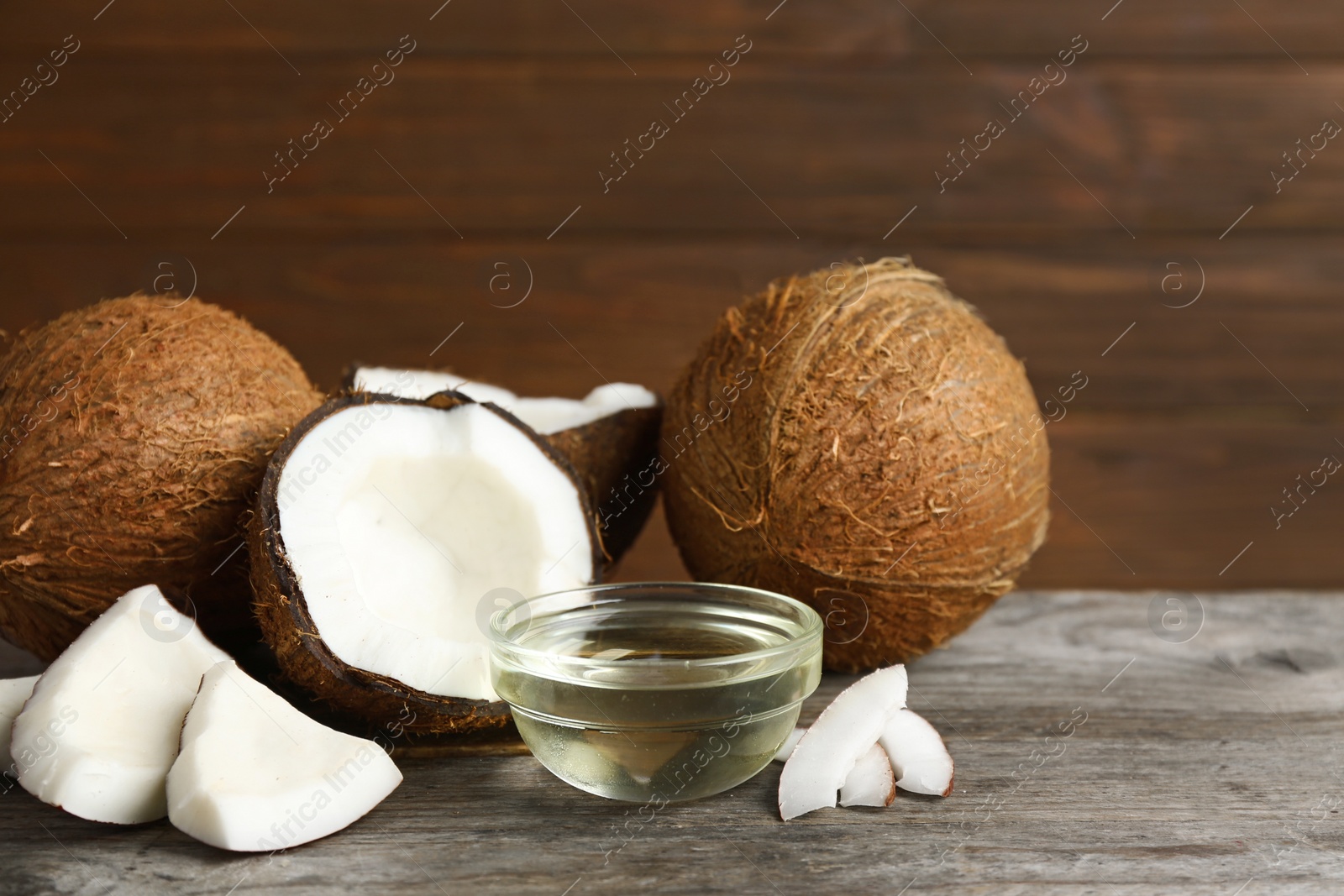 Photo of Bowl of natural organic oil and coconuts on brown wooden table