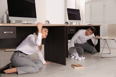 Photo of Scared employees hiding under office desks during earthquake