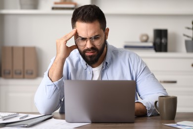 Photo of Man with glasses suffering from headache at workplace in office