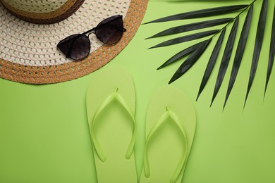 Photo of Stylish flip flops, sunglasses, hat and palm leaf on light green background, flat lay