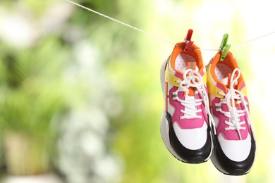 Photo of Stylish sneakers drying on washing line against blurred background, space for text