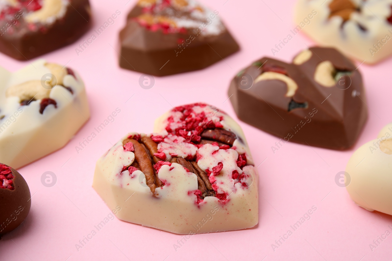 Photo of Tasty chocolate heart shaped candies with nuts on pink background, closeup