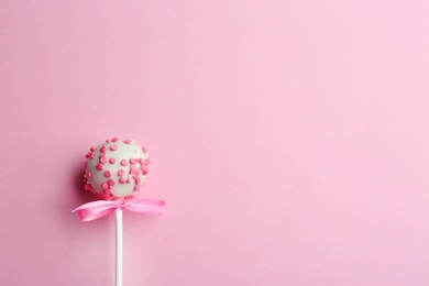 Tasty cake pop with bow on light pink background, top view. Space for text