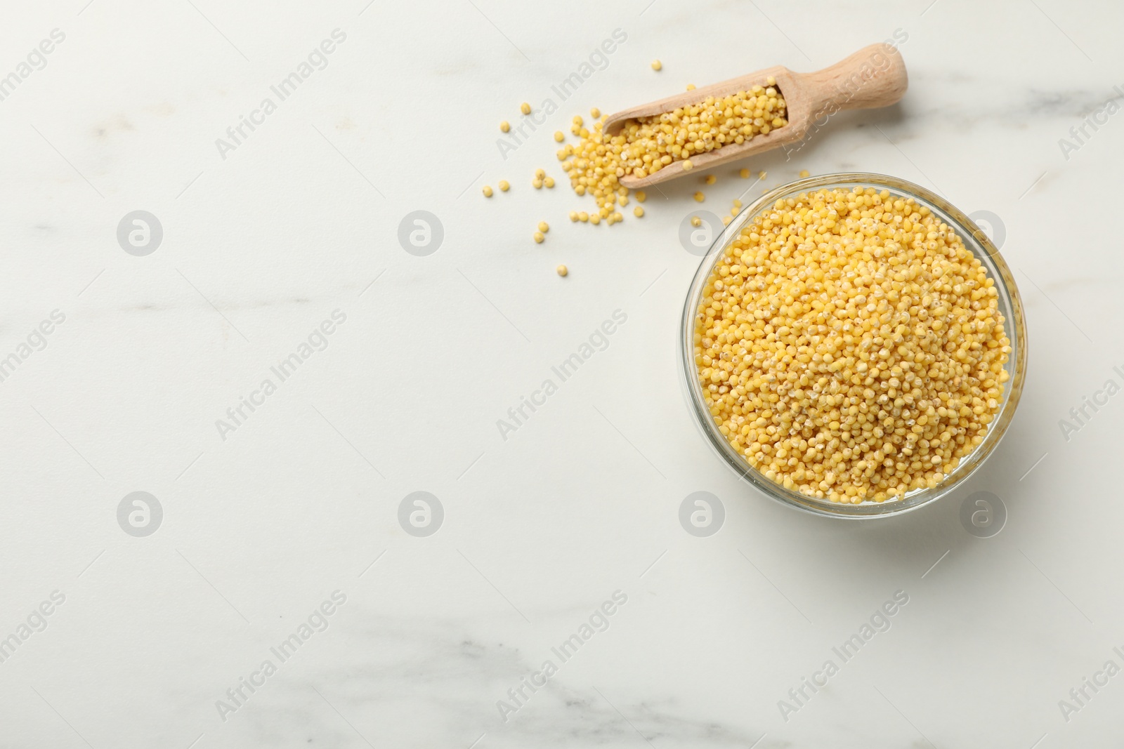 Photo of Millet groats in bowl and scoop on white marble table, flat lay. Space for text