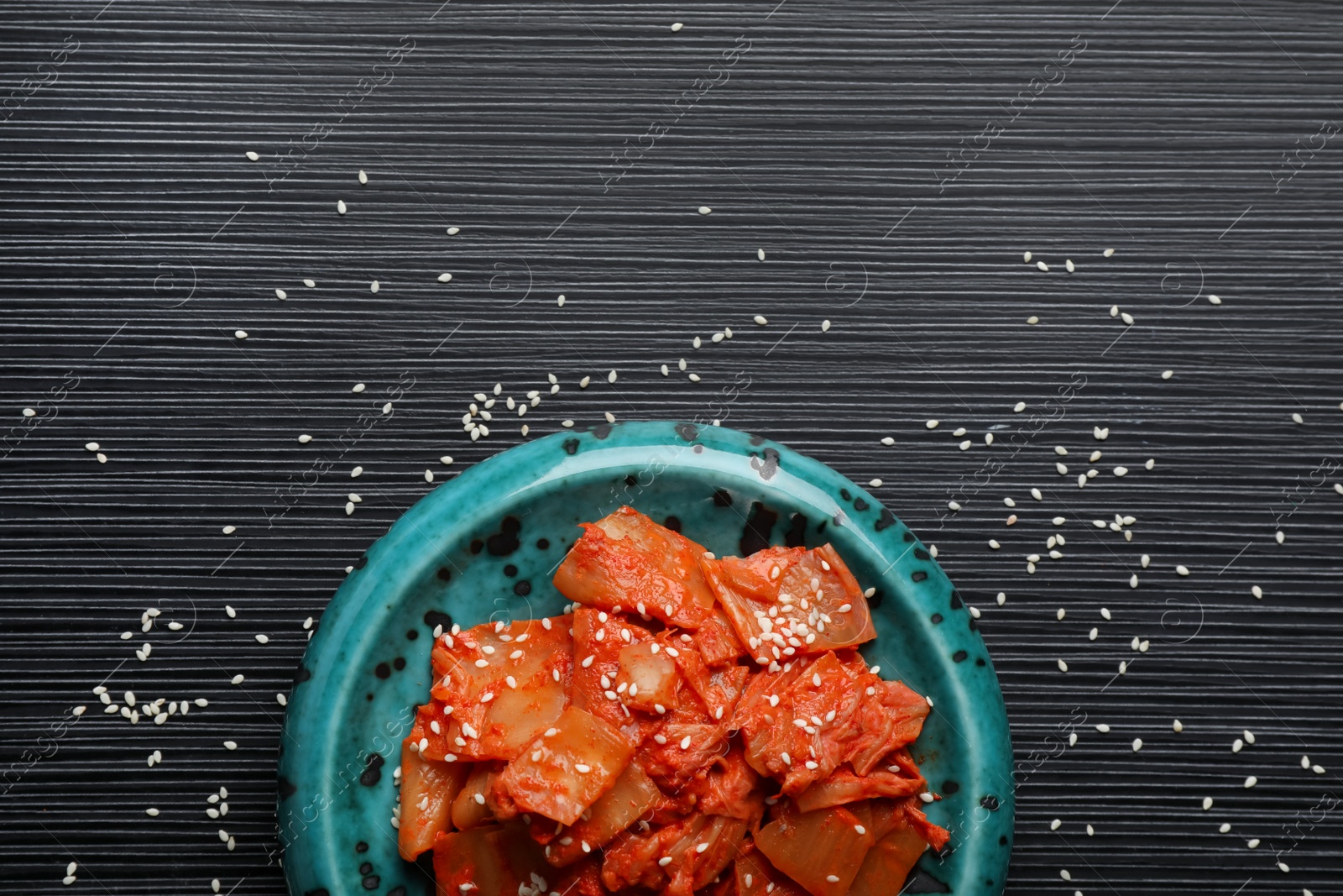 Photo of Plate of spicy cabbage kimchi and sesame seeds on black wooden table, flat lay. Space for text