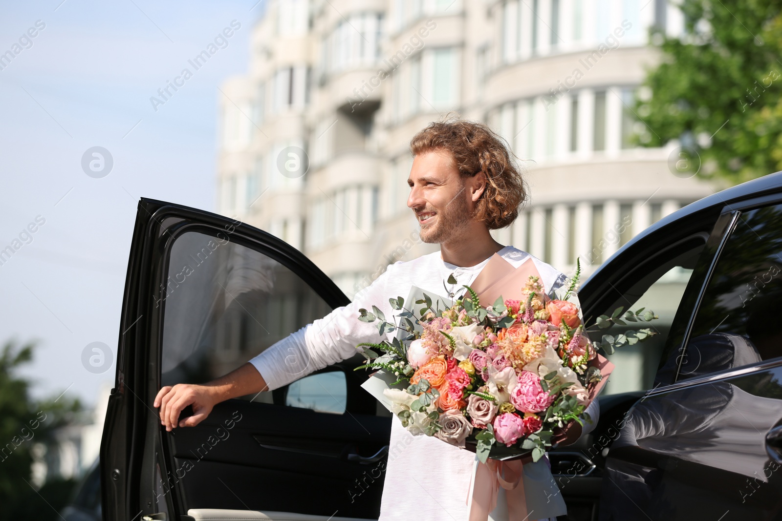 Photo of Young handsome man with beautiful flower bouquet near car on street